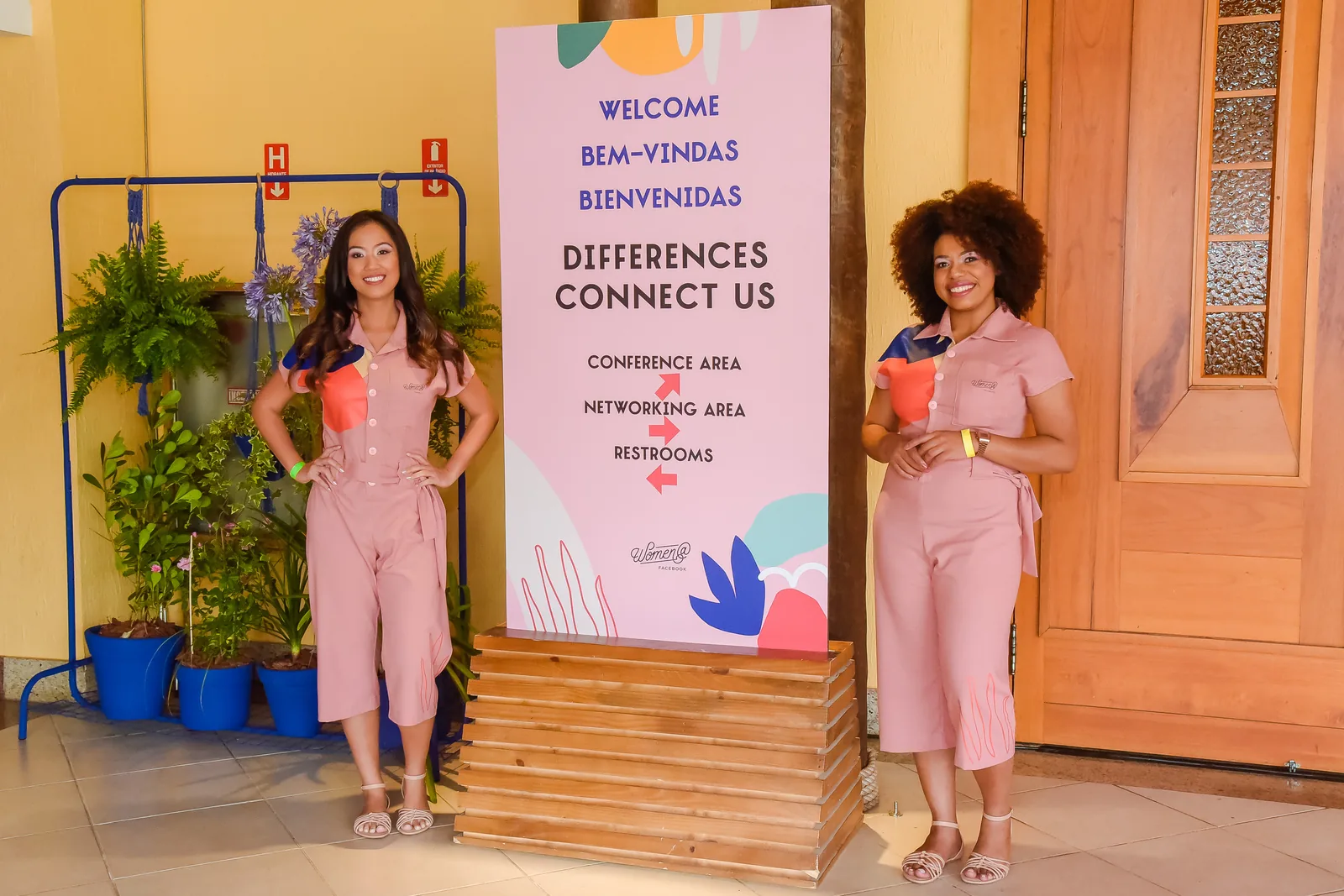 Two team members in the pink jumpsuit next to the welcome sign