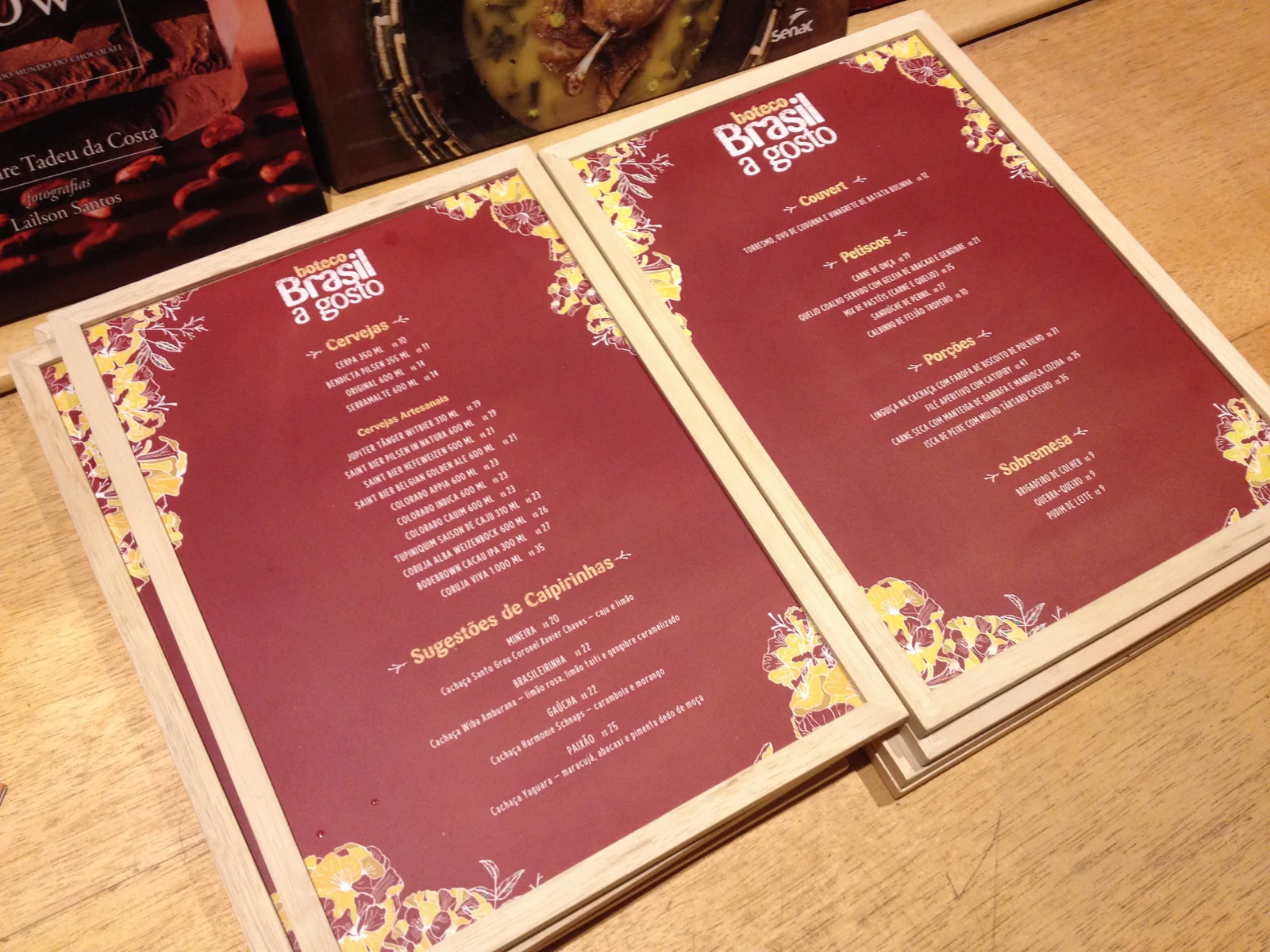Printed boteco menus on deep red, framed by the ipê