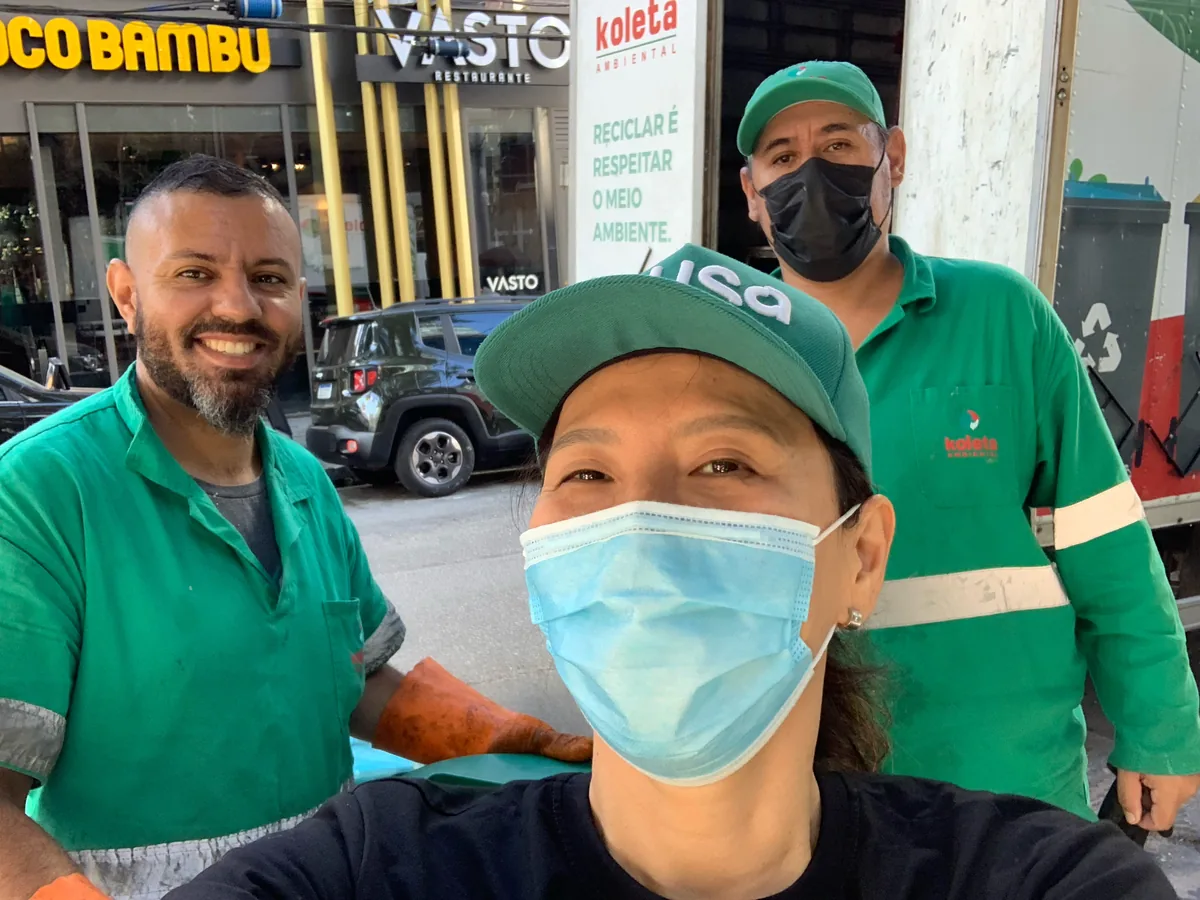 Selfie on a collection route: Yuki in a Musa cap and face mask with two collection workers in green uniforms, next to the truck