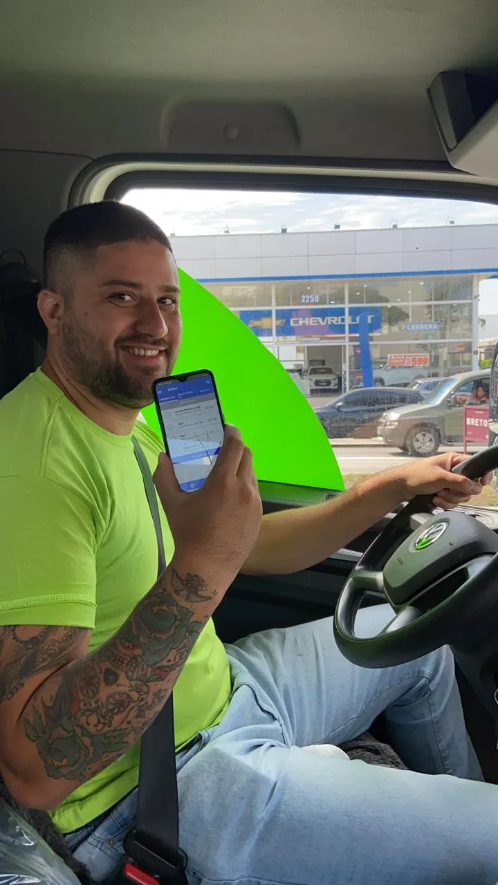 A driver in his truck cab holding up the app on his own phone